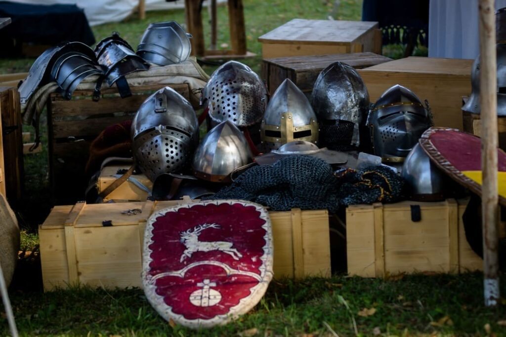 Mehrere mittelalterliche Helme, Kettengeflecht und bemalte Schilde liegen beim Burg Stettenfels Mittelalterfest auf Holzkisten ausgestellt.
