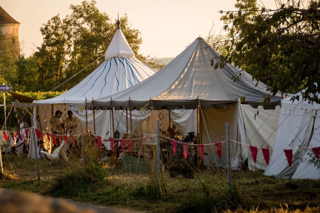 Mehrere große weiße Mittelalterzelte stehen beim Burg Stettenfels Mittelalterfest auf einer Wiese, geschmückt mit roten Wimpeln.
